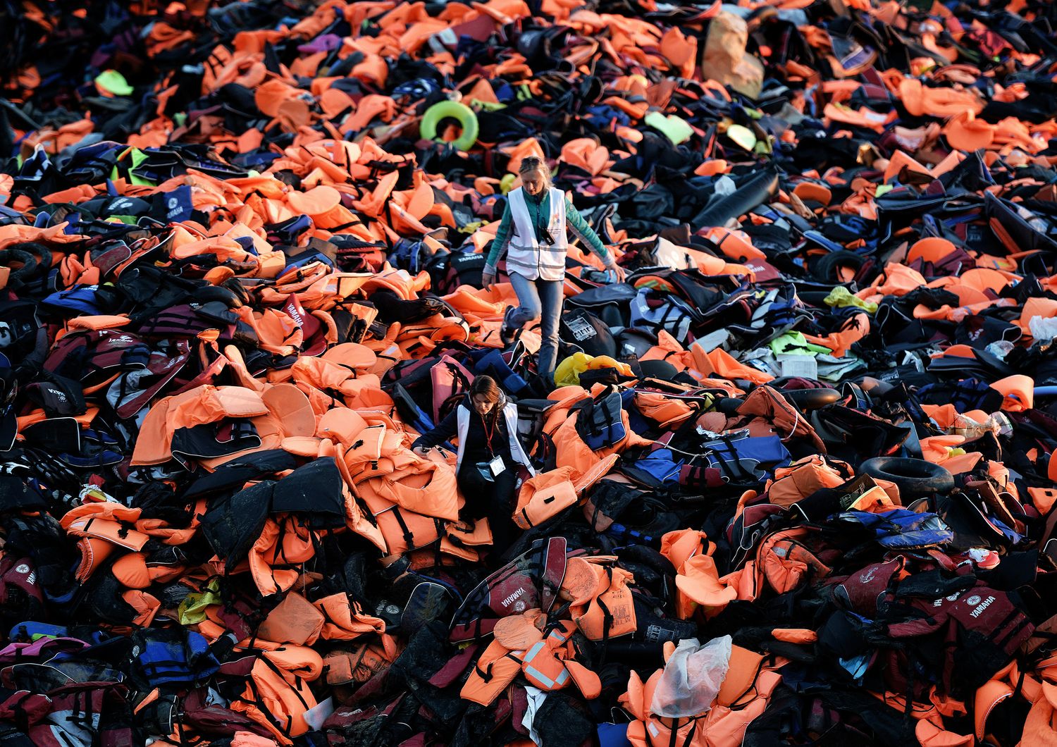 &nbsp;Volontari camminano su un mucchio di giubbotti di salvataggio lasciati da rifugiati e migranti arrivatinell'isola greca di Lesbo dopo aver attraversato il mare Egeo dalla Turchia (3 dicembre 2015)