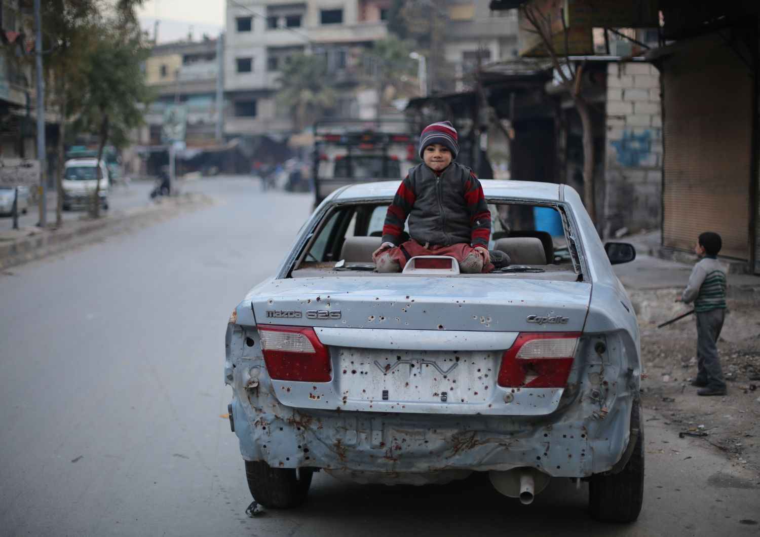 Un bambino su una vettura danneggiata da un'esplosione nel Ghouta orientale (foto Amer Al Shami per Save the Children)&nbsp;