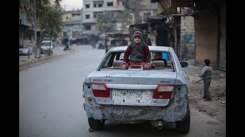 Un bambino su una vettura danneggiata da un'esplosione nel Ghouta orientale (foto Amer Al Shami per Save the Children)&nbsp;