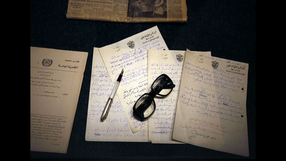 Vecchi occhiali e una penna stilografica che giace sulla cima di documenti scritti a mano che portano il sigillo del movimento Fatah (C), un vecchio giornale (in alto) in mostra presso il nuovo Museo Arafat nella citt&agrave; cisgiordana di Ramallah (Afp)&nbsp;
