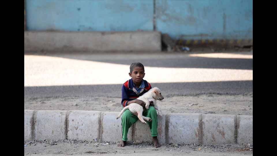 Un bambino indiano seduto con il suo cucciolo ai margini di una strada (Foto Afp)&nbsp;