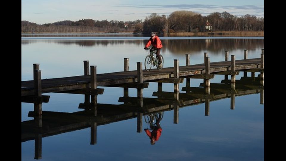 &nbsp;Un ciclista pedala su un ponte sul lago di Woerthsee vicino al villaggio di Inning in Germania (Foto Afp)