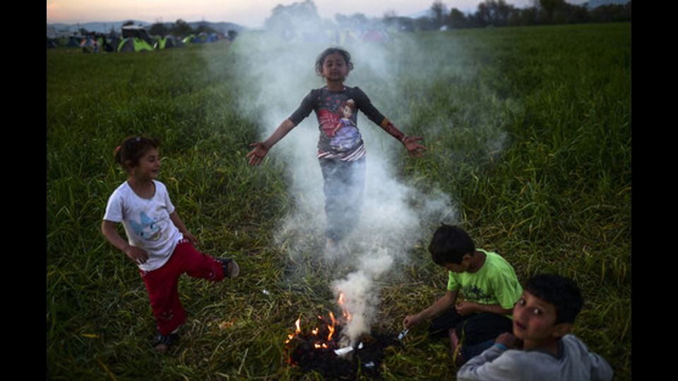 I bambini si riuniscono intorno a un fal&ograve; in un campo improvvisato al confine greco-macedone, nei pressi del villaggio greco di Idomeni, dove oltre 11.000 di rifugiati e migranti erano bloccati dalla chiusura della frontiera balcanica (31 marzo 2016) (foto Afp) &nbsp;