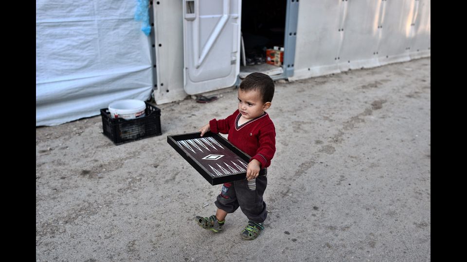 Un bambino porta un gioco in un campo di fortuna sull'isola di Chios, Grecia (13 ottobre 2016) (foto Afp)&nbsp;