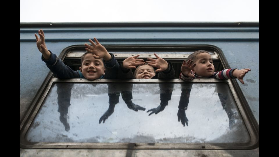 Tre bambini allungano le braccia mentre aspettano che altri migranti e rifugiati salgano sul treno diretto in Serbia da Gevgelija, cittadina macedone al confine con la Grecia. (foto Afp)
