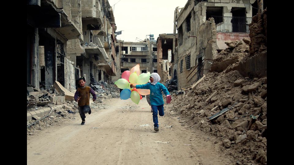 Bambini siriani corrono con i palloncini tra le macerie di Jobar, alla periferia della capitale, Damasco. La foto &egrave; stata scattata il 9 aprile 2016 (foto Afp)