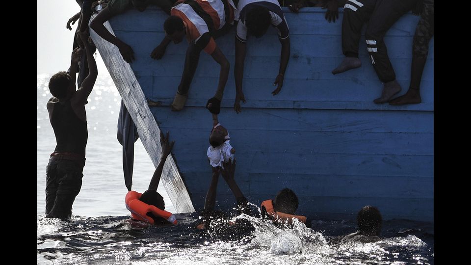 Profughi che cercano di salvare un bambino nelle acque al nord della Libia (foto Afp)