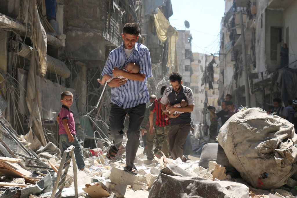 Guerra in Siria: un uomo tiene in braccio un bambino tra le macerie e i palazzi distrutti di Aleppo (foto Afp)&nbsp;