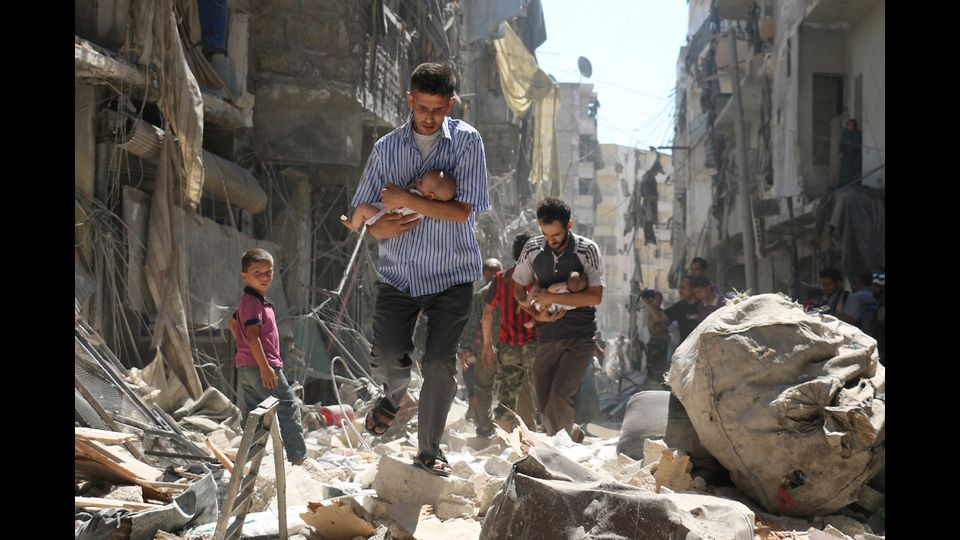 Guerra in Siria: un uomo tiene in braccio un bambino tra le macerie e i palazzi distrutti di Aleppo (foto Afp)&nbsp;
