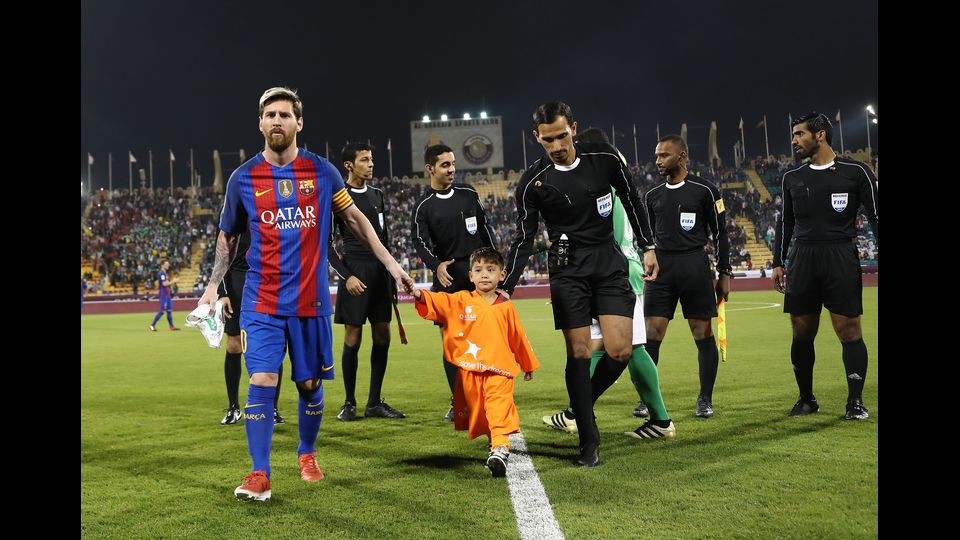 Messi in campo mano nella mano con il piccolo Murtaza prima di un'amichevole a Doa tra Barcellona e Al-Ahli. La foto del ragazzino afghano con un sacchetto della spesa dipinto di bianco e azzurro, col numero 10 della Pulce, aveva fatto il giro del mondo&nbsp;