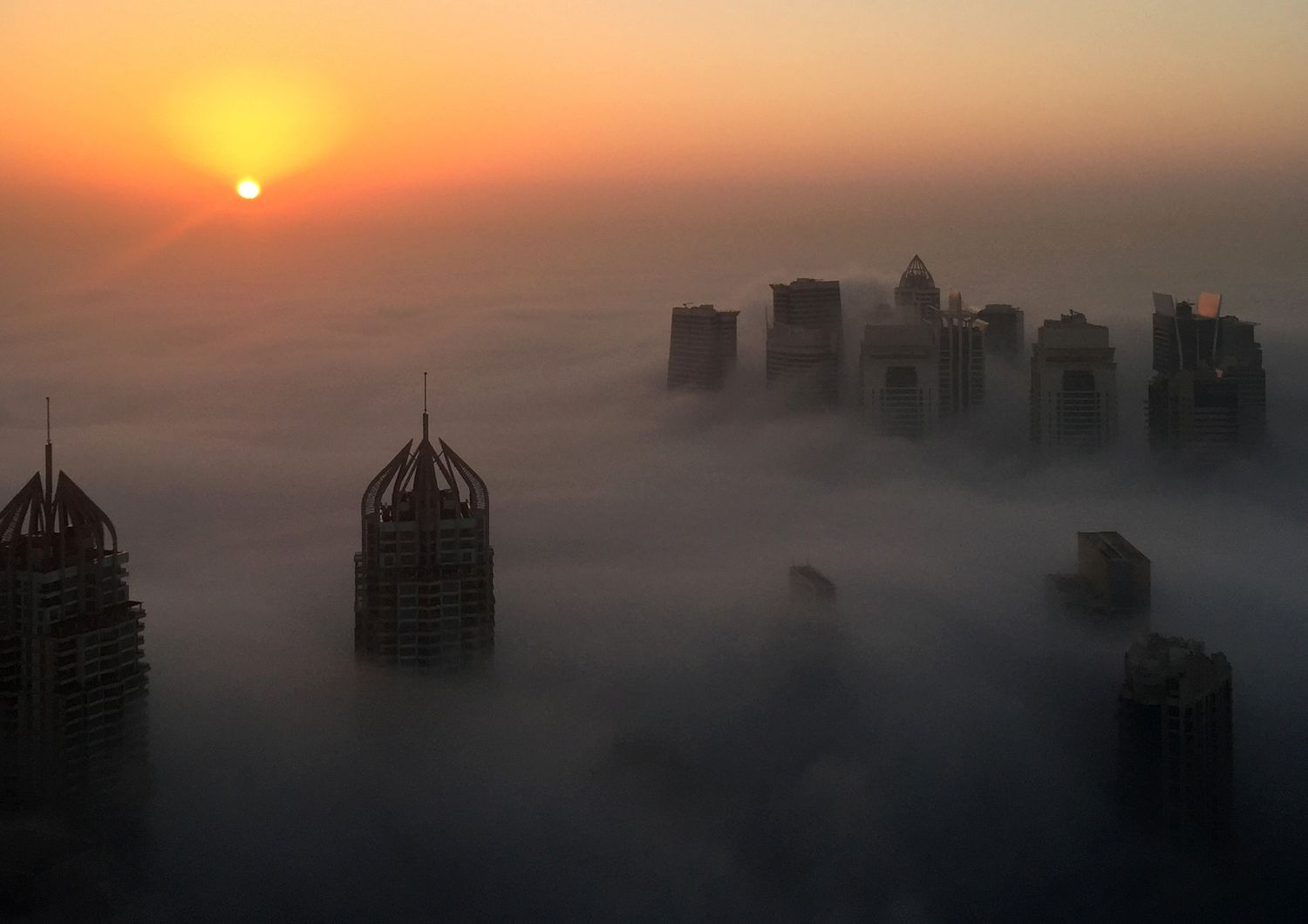 Dubai. Il sole sorge dietro i grattaceli 'immersi' tra le nuvole e una fitta coltre di nebbia