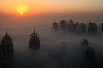 Dubai. Il sole sorge dietro i grattaceli 'immersi' tra le nuvole e una fitta coltre di nebbia