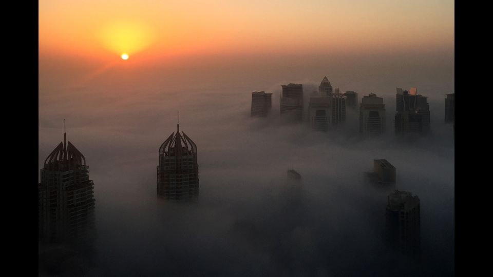 Dubai. Il sole sorge dietro i grattaceli 'immersi' tra le nuvole e una fitta coltre di nebbia