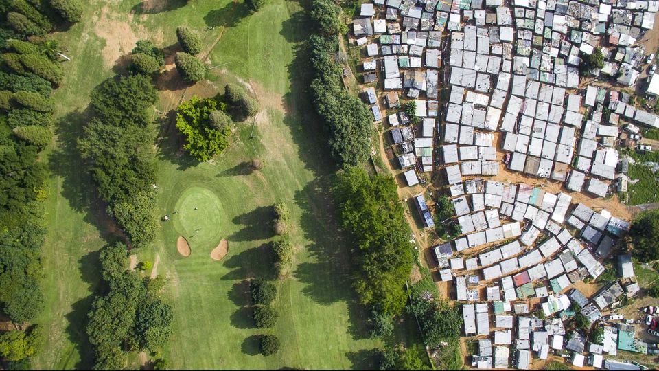 Nella foto il campo da golf Papwa Sewgolum di Durban, Sudafrica.   Sewsunker&nbsp;Sewgolum detto &ldquo;Papwa&rdquo; &egrave; stato il primo nero a partecipare al Natal Open, torneo di golf sudafricano che si &egrave; tenuto dal 1925 al 1975. Figlio di lavoratori nei campi di canne da zucchero, gioc&ograve; nel torneo per la prima volta nel 1961. Papwa non si limit&ograve; a partecipare, ma vinse nel 1963 e ancora nel 1965, anno in cui era l&rsquo;unico concorrente di colore. Gli altri 113 erano tutti bianchi.Per via dell'apartheid allora in vigore nel Paese, la cerimonia di premiazione si tenne fuori dalla struttura sportiva, mentre pioveva; all'interno, tutti i suoi avversari bianchi erano seduti comodi e al riparo.&nbsp; In suo onore il campo da golf porta ora il suo nome. Ma quella che dovrebbe essere una storia di rivincita sociale non &egrave; ancora pienamente compiuta: il campo di gioco &egrave; circondato da umilissime baracche. Una ringhiera separa le due realt&agrave;.&nbsp;
