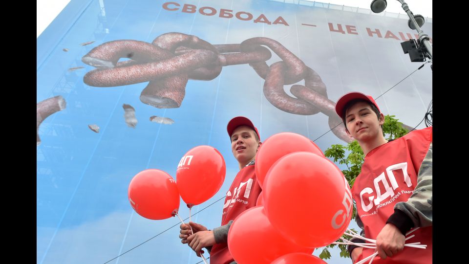 Ucraina - Giovani attivisti portano palloncini rossi davanti a un cartellone che raffigura catene con scritto &quot;La libert&agrave; &egrave; la nostra religione&quot; alla manifestazione per il 1 maggio, organizzata dai partiti ucraini di sinistra e dai sindacati a Kiev (Afp)&nbsp;