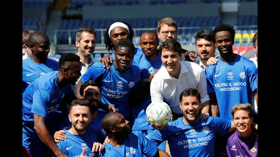 Justin Trudeau con il pallone in mano, posa con i giocatori di calcio della squadra dei migranti e dei rifugiati liberi di Nantes prima della partita &quot;Obiettivo aperto&quot; (Afp)