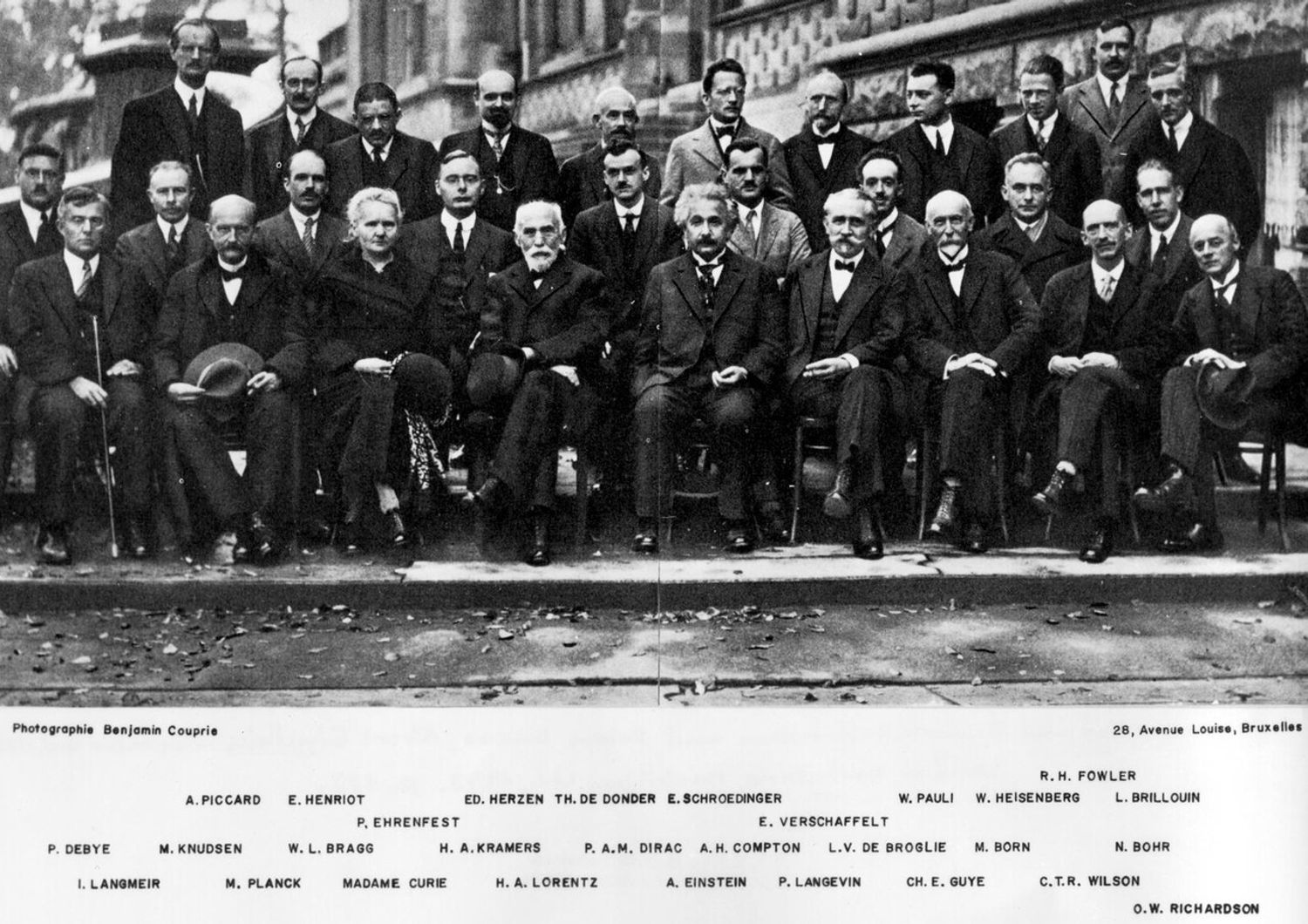 In piedi, in terza fila: A. Piccard, E. Henriot, P. Ehrenfest, E. Herzen, Th. de Donder, E. Schr&ouml;dinger, J.E. Verschaffelt, W. Pauli, W. Heisenberg, R. Fowler, L. Brillouin; Nella fila centrale: P. Debye, M. Knudsen, W.L. Bragg, H.A. Kramers, P.A.M. Dirac, A.H. Compton, L. de Broglie, M. Born, N. Bohr; Seduti davanti: I. Langmuir, M. Planck, M. Skłodowska-Curie, H.A. Lorentz, A. Einstein, P. Langevin, Ch.-E. Guye, C.T.R. Wilson, O.W. Richardson.