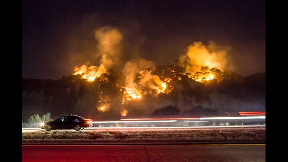 Una macchina sfreccia mentre il Thomas Fire brucia una collina a sud di Casitas Springs in California
