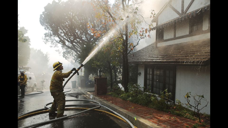 Un vigile del fuoco getta l'acqua sugli alberi vicino ad una casa che brucia nella vicinanza ricca di Bel-Air durante il fuoco di Skirball.