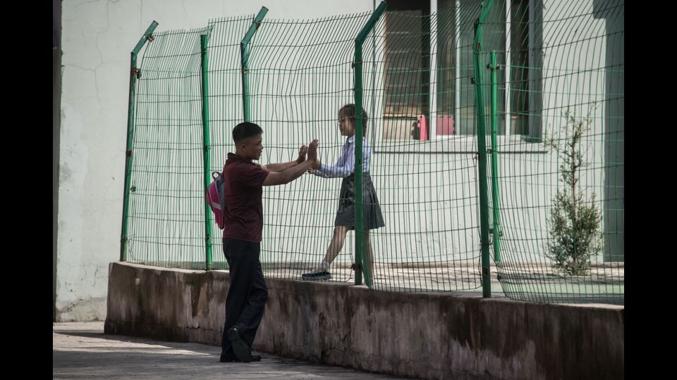 Un uomo e una bambina parlano attraverso una rete fuori da una scuola a Pyongyang