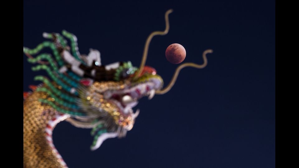 La super Luna rossa e blu spunta sopra la testa di una statua di un drago cinese in un tempio buddista a Bangkok, in Thailandia&nbsp;