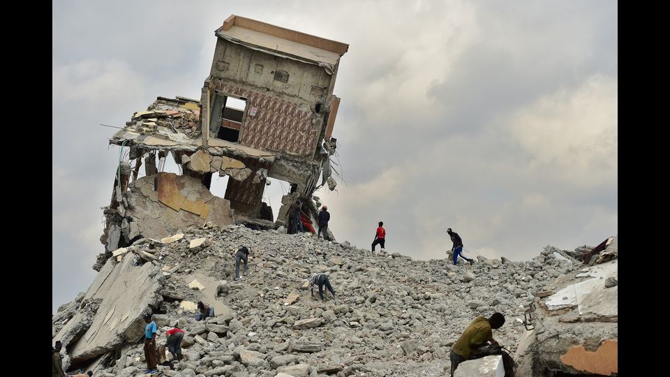 Un gruppo di persone recupera materiale da costruzione il 13 settembre 2018, in un sito di demolizione con macerie precariamente inclinate, dopo che i bulldozer governativi hanno abbattuto un centro commerciale accusato di essere illegale per essere stato costruito su un letto del fiume nella capitale del Kenya, Nairobi.TONY KARUMBA / AFP