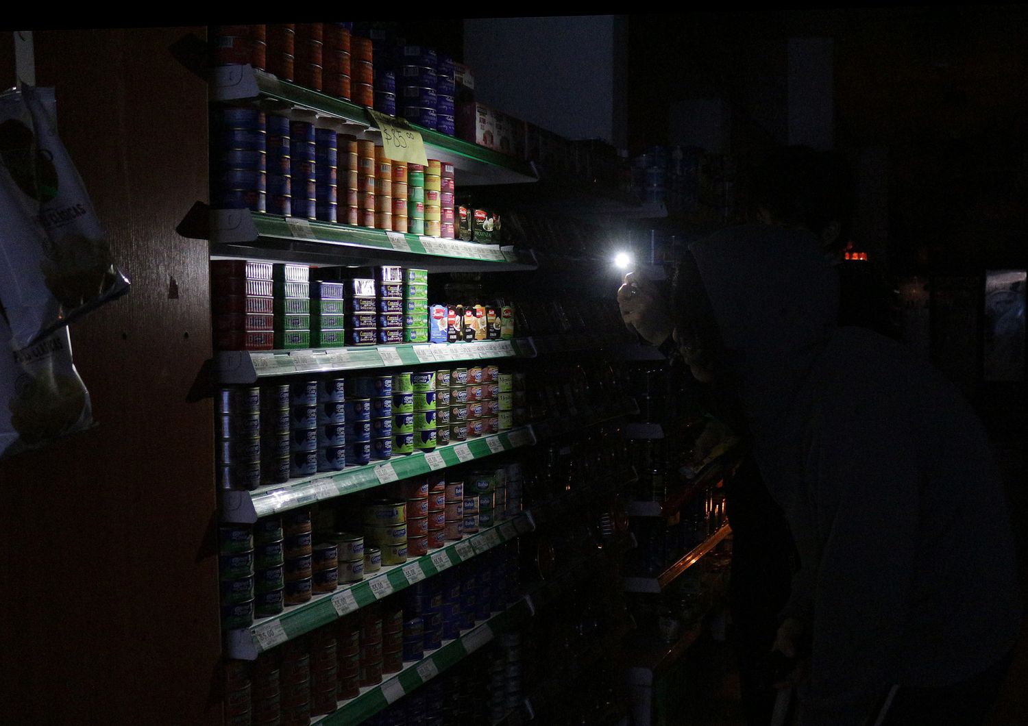 Un cliente si fa luce con uno smartphone tra gli scaffali di un supermercato di Buenos Aires durante il blackout
