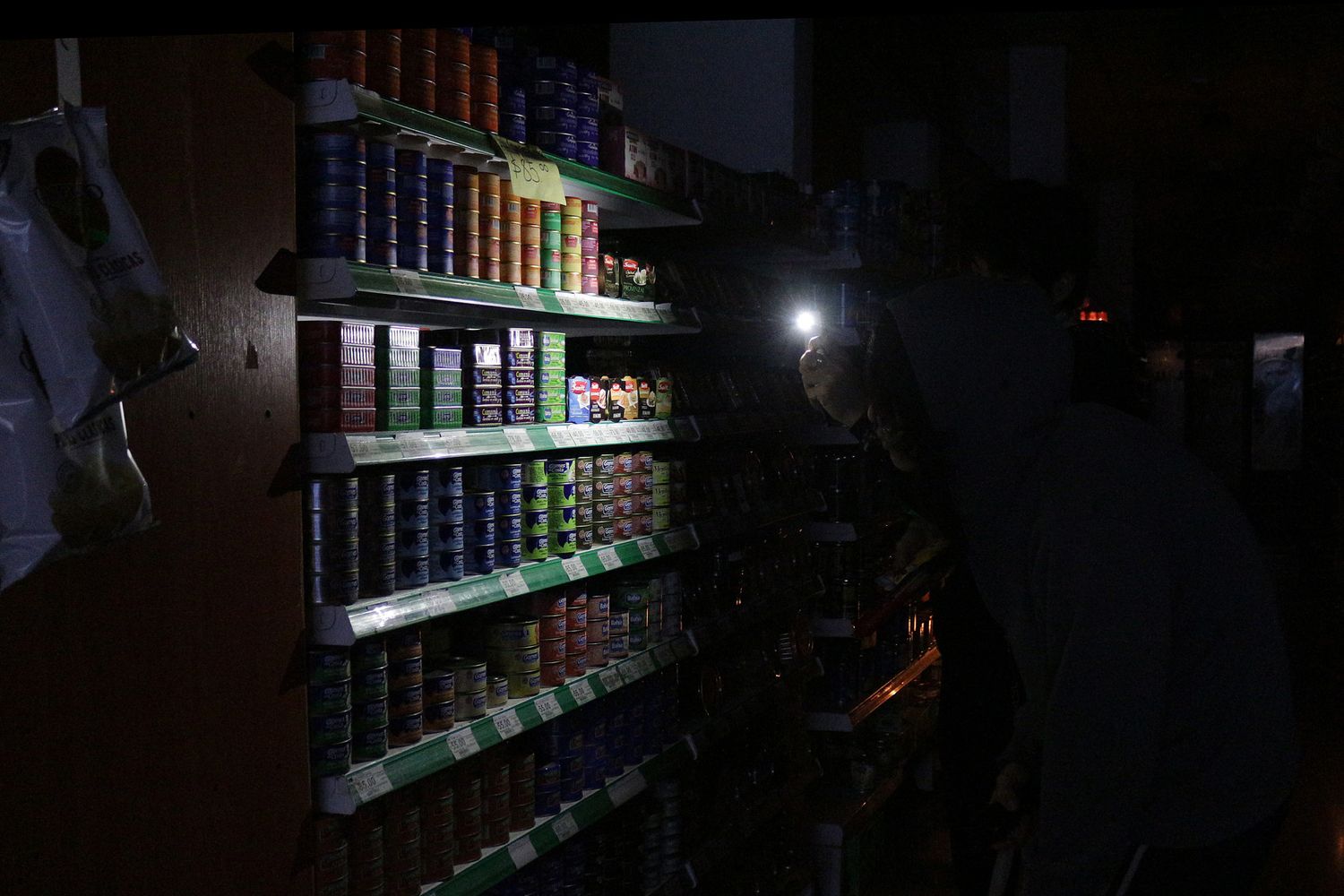 Un cliente si fa luce con uno smartphone tra gli scaffali di un supermercato di Buenos Aires durante il blackout