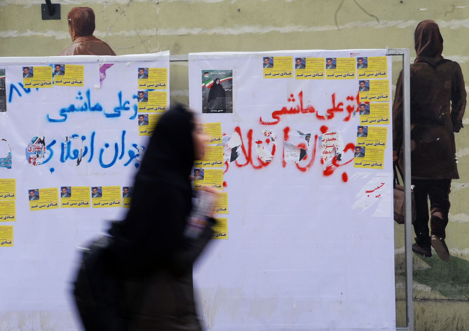 Una donna cammina davanti ai manifesti elettorali a Teheran