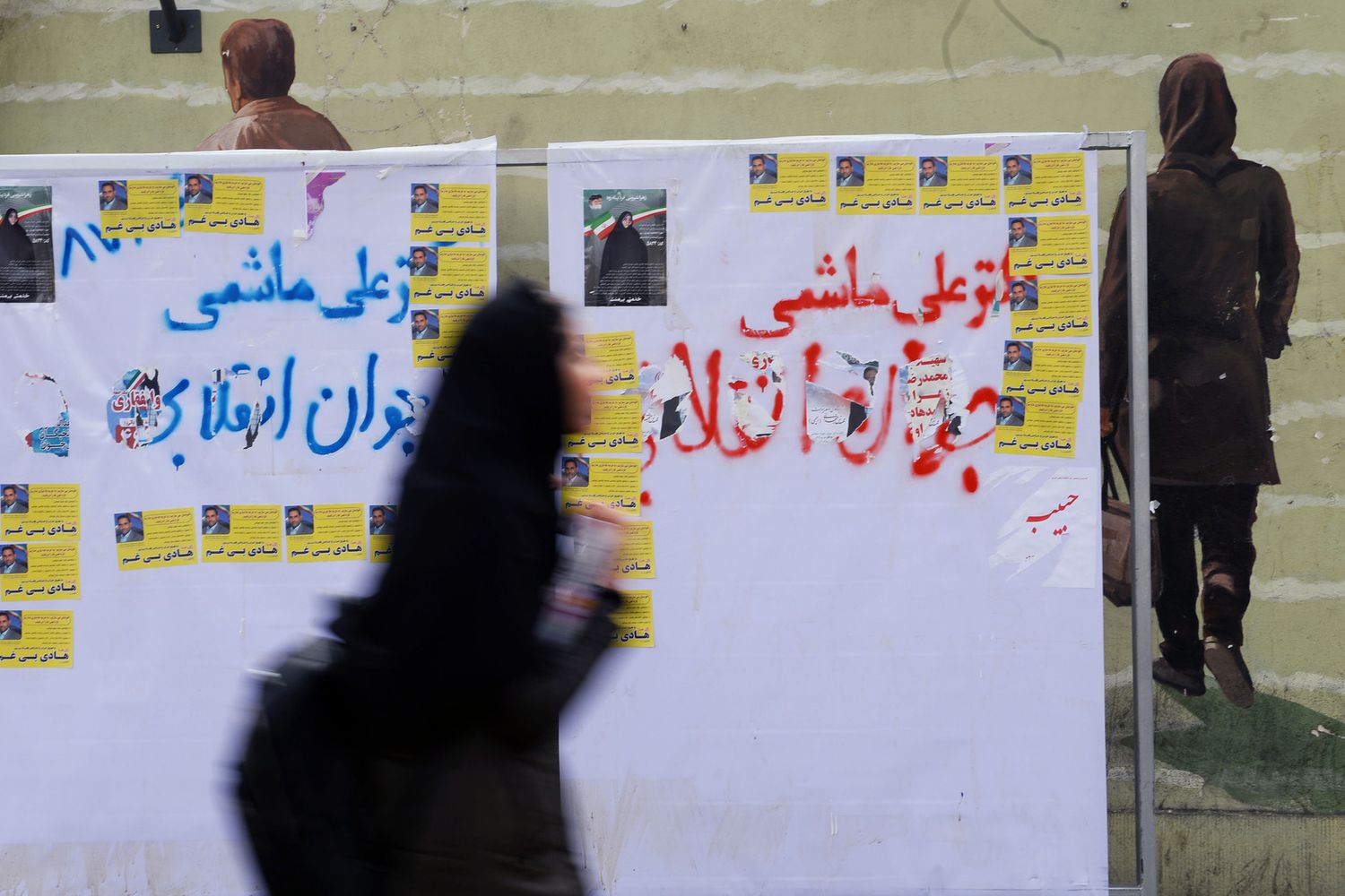 Una donna cammina davanti ai manifesti elettorali a Teheran