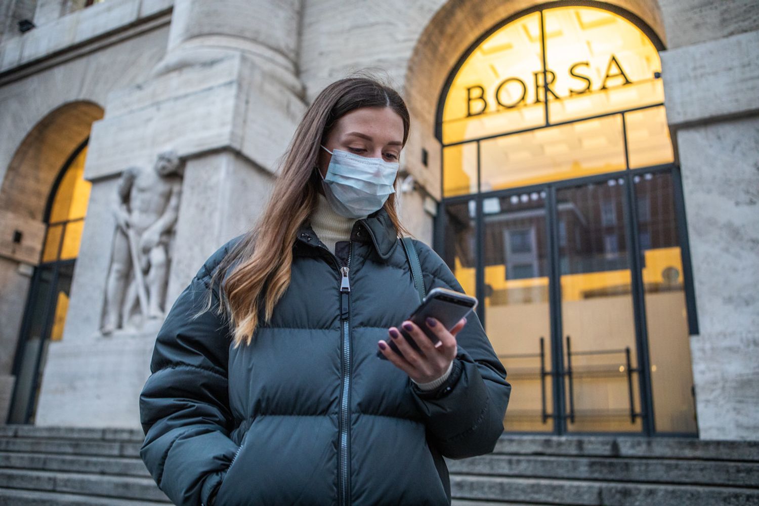 Una donna con mascherina protettiva di fronte alla Borsa di Milano