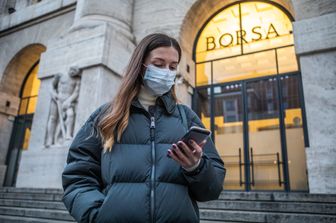 Una donna con mascherina protettiva di fronte alla Borsa di Milano