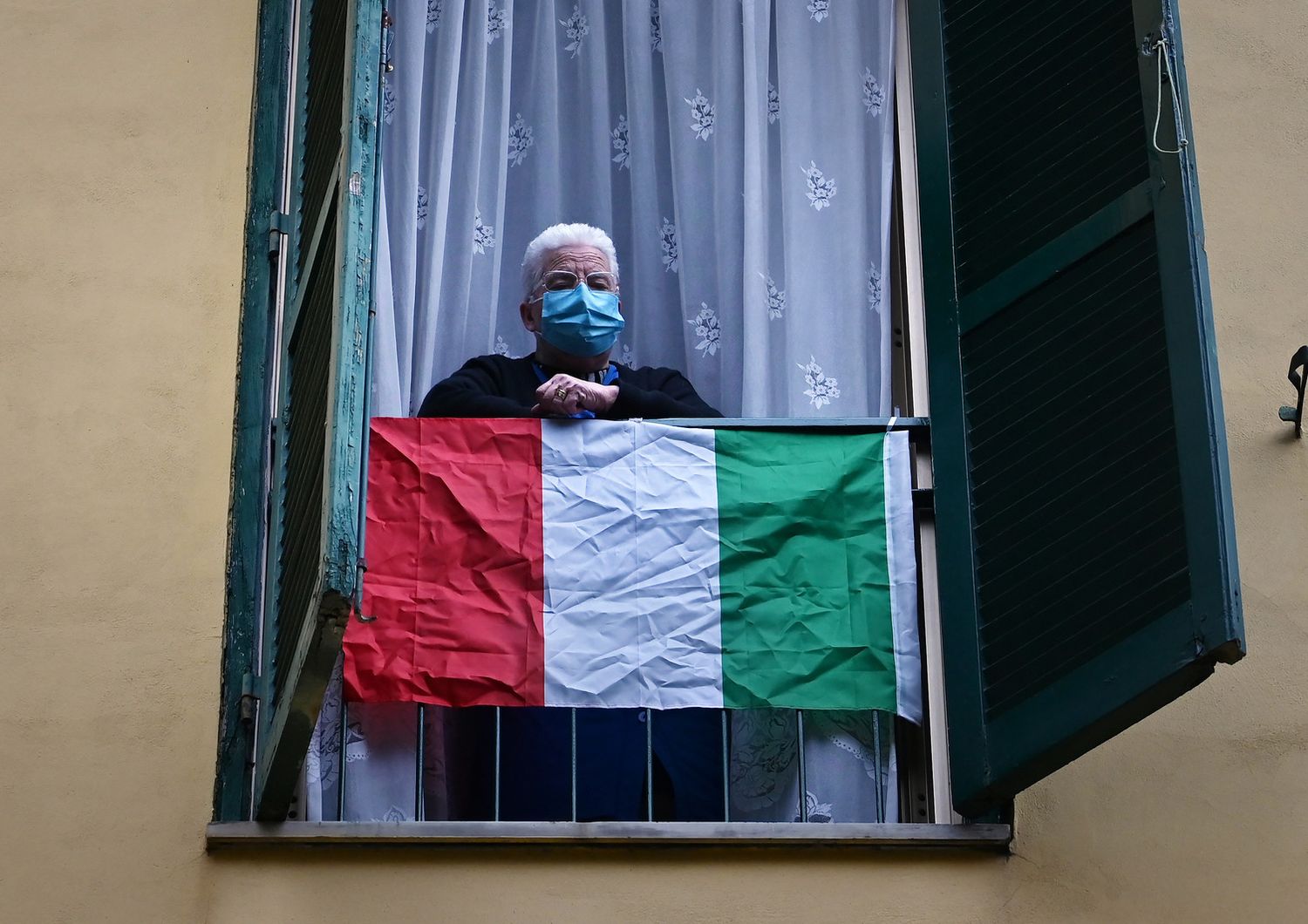 Un anziano con la mascherina protettiva contro il coronavirus sul balcone di casa a Roma