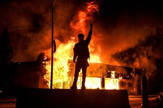 Un manifestante di fronte a un edificio in fiamme a Minneapolis