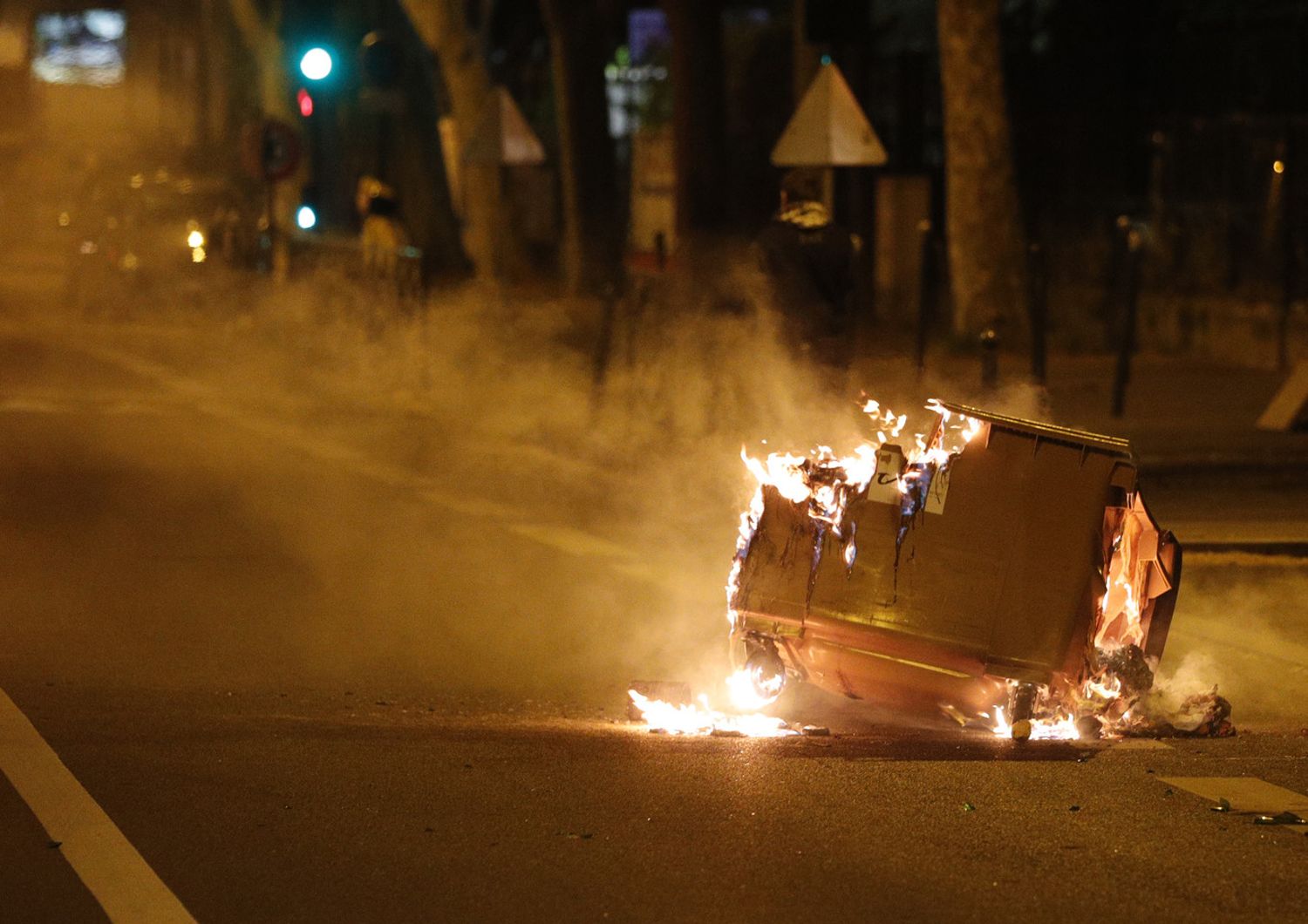 Un cassonetto brucia in strada a Parigi durante disordini tra manifestanti e polizia