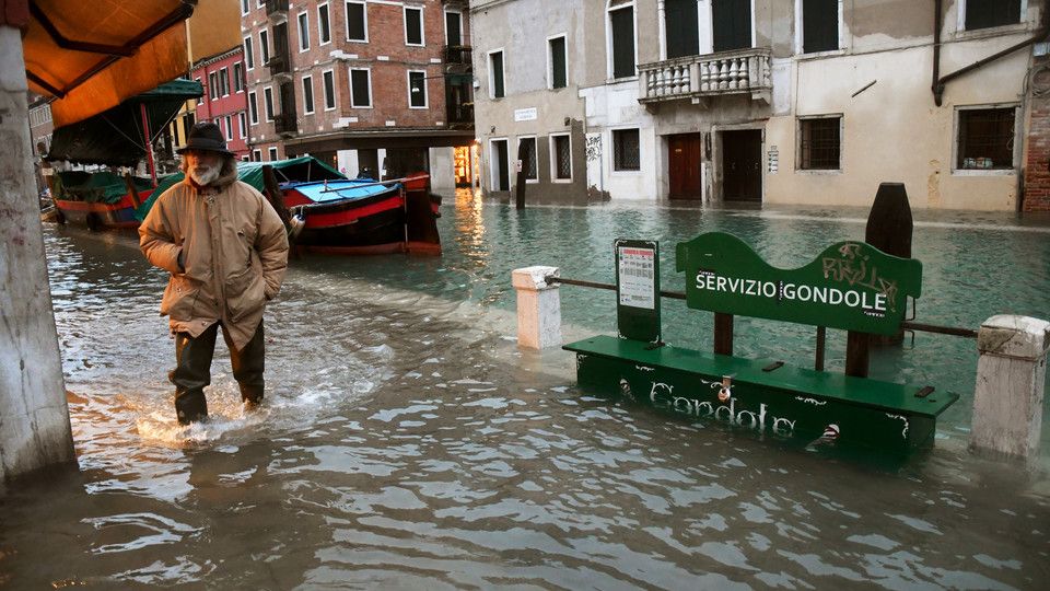 Un uomo attraversa un canale gonfiato dall'acqua alta