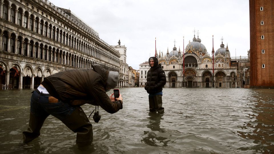 Passanti scattano foto ricordo nello scenario di piazza San Marco con l'acqua alta