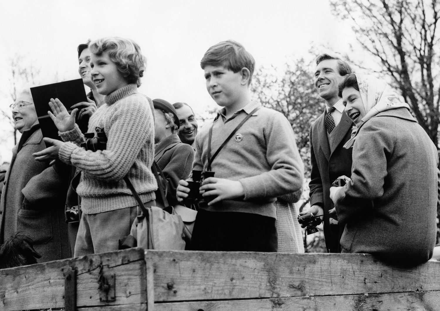La regina Elisabetta, con il capo coperto da un foulard, assiste a una gara campestre nel 1961 a Badminton. In primo piano, col binocolo, il principe Carlo