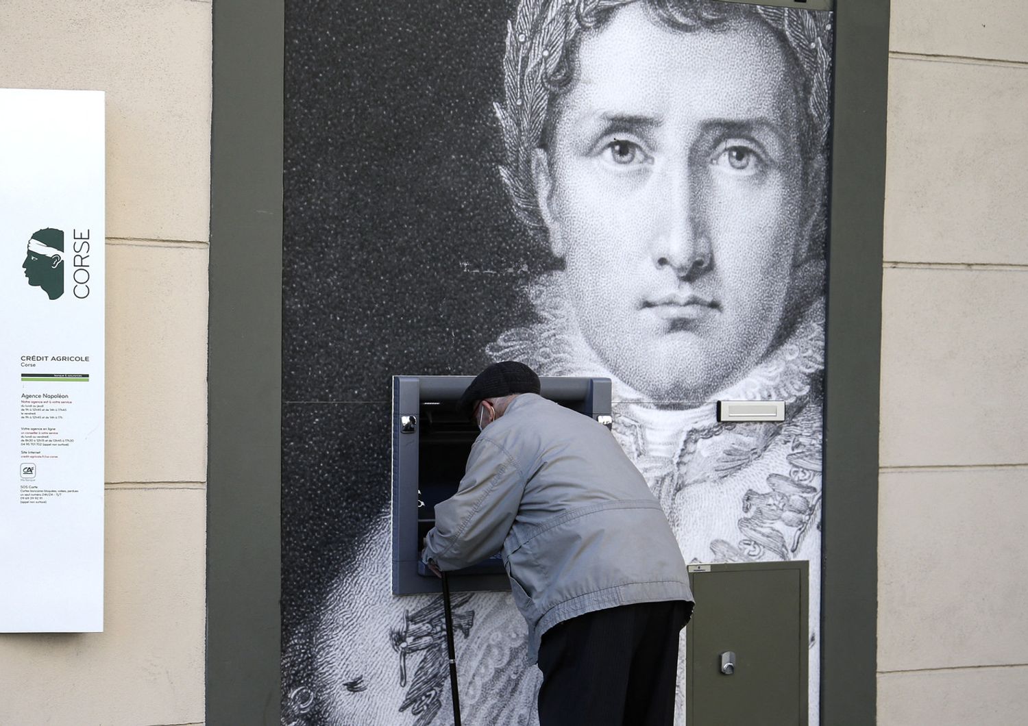 Un uomo preleva denaro da una bancomat decorato con il ritratto di Napoleone ad Ajaccio