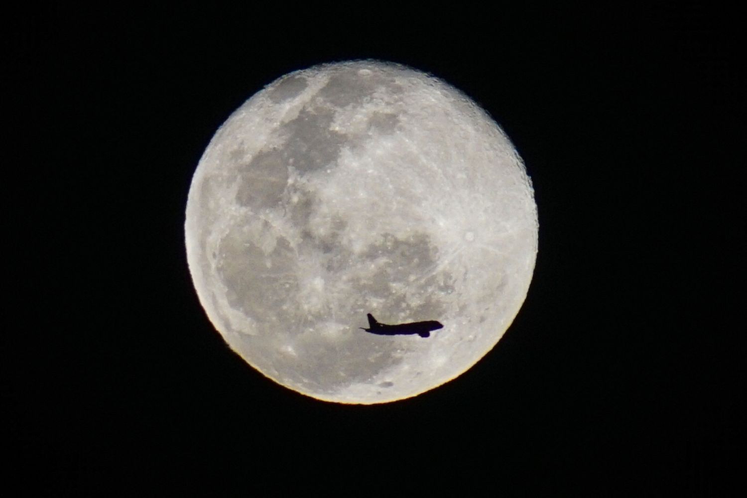 La sagoma di un aereo si staglia contro la Luna
