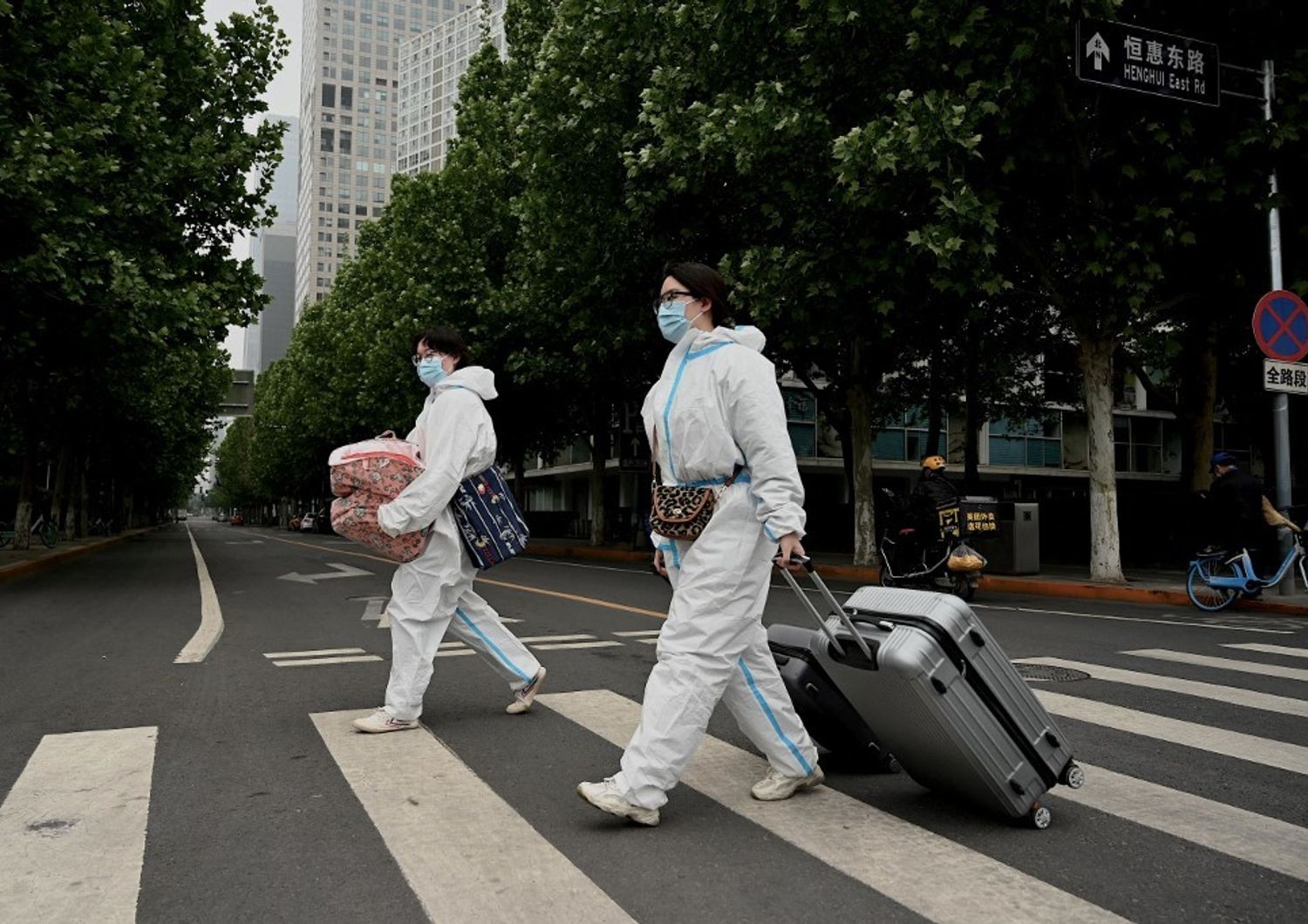 Persone che indossano dispositivi di protezione individuale attraversano una strada con i loro bagagli vicino a un'area bloccata