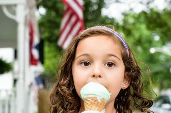 Una bambina mangia il gelato con la bandiera americana sullo sfondo
