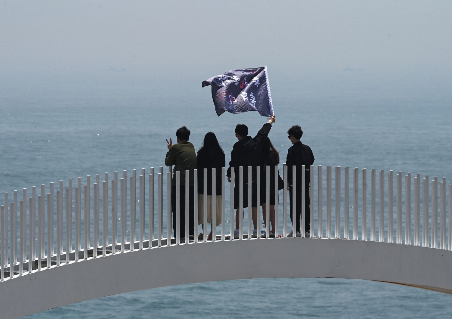 Turisti cinesi sventolano una bandiera su un ponte che si affaccia sullo stretto di Taiwan