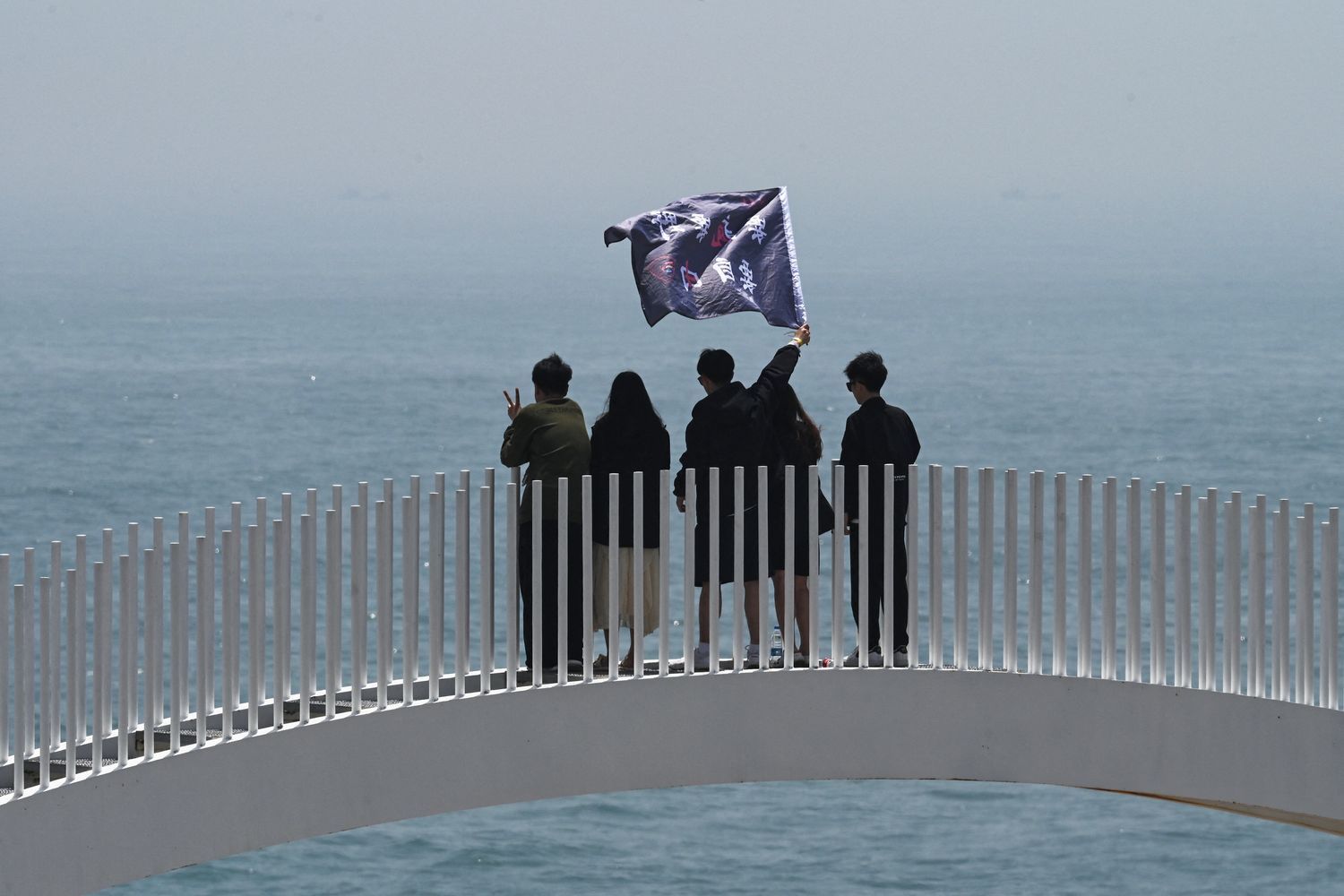 Turisti cinesi sventolano una bandiera su un ponte che si affaccia sullo stretto di Taiwan