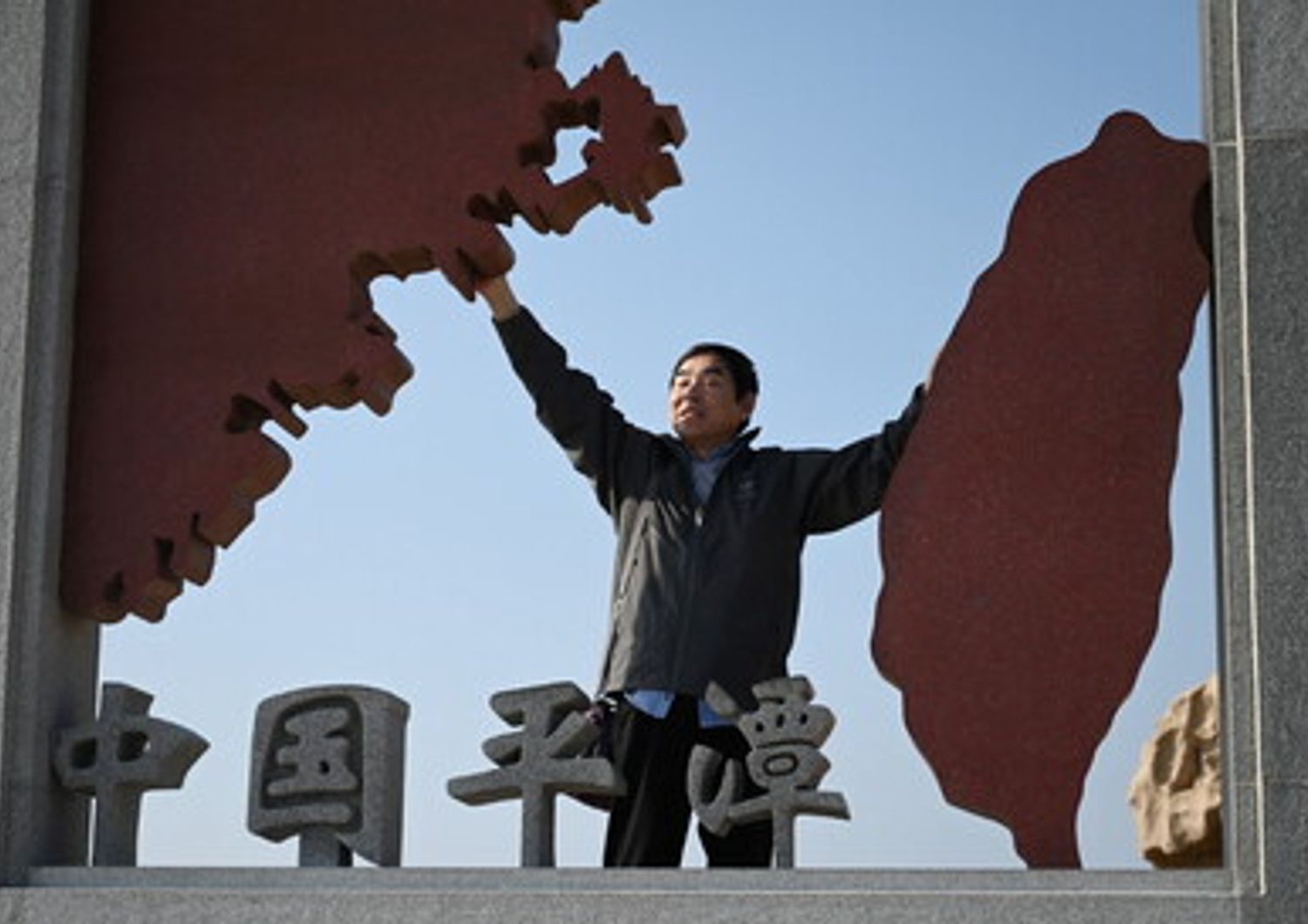 Un uomo posa in una scultura raffigurante Taiwan (a destra) e la Cina continentale (a sinistra), sull'isola di Pingtan&nbsp;
