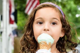 Una bambina mangia il gelato con la bandiera americana sullo sfondo
