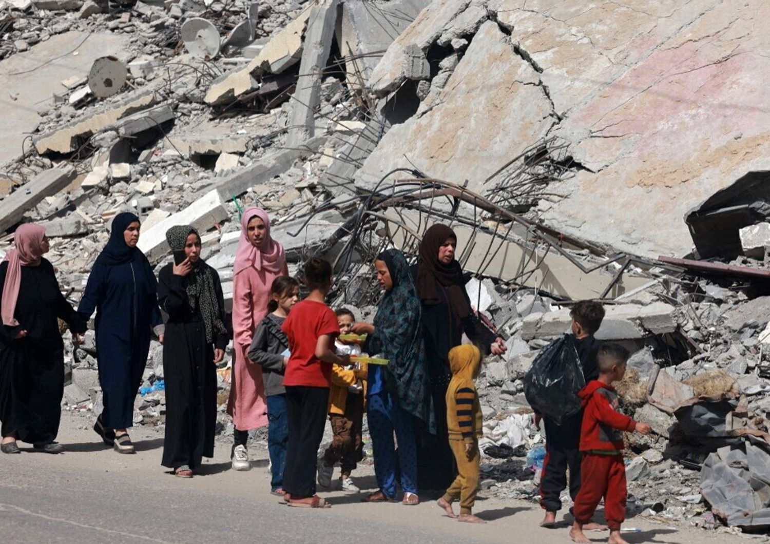 Donne e bambini palestinesi camminano vicino a un edificio distrutto da un bombardamento israeliano a Rafah, nel sud della Striscia di Gaza, il 31 marzo 2024