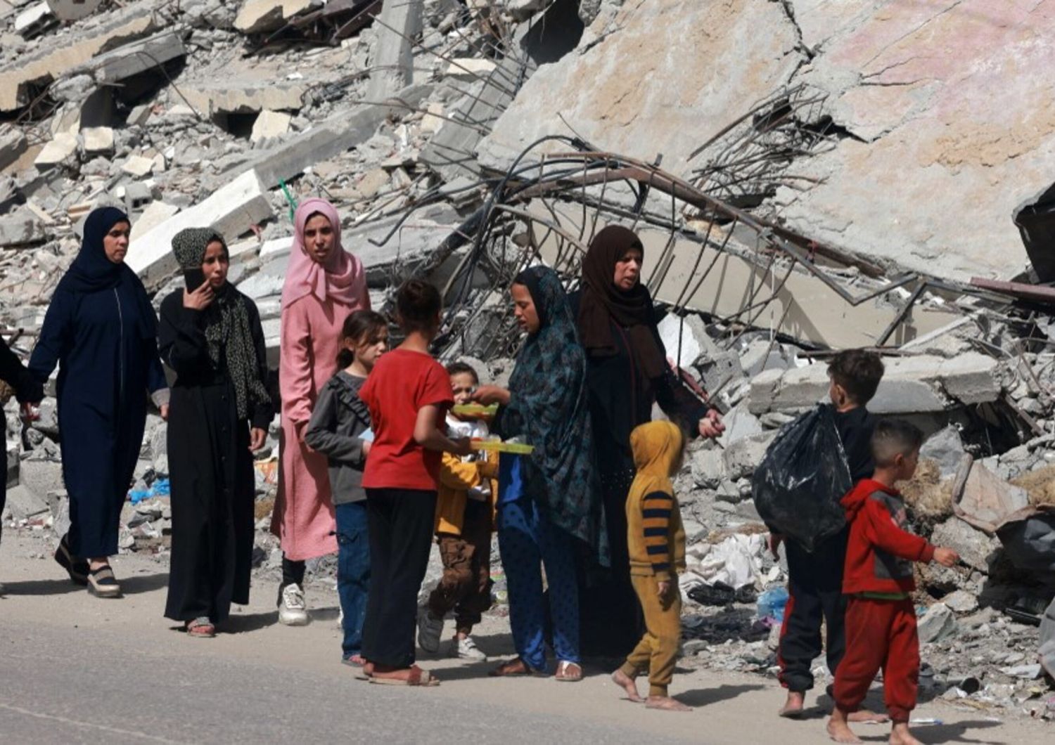 Donne e bambini palestinesi camminano vicino a un edificio distrutto da un bombardamento israeliano a Rafah, nel sud della Striscia di Gaza, il 31 marzo 2024