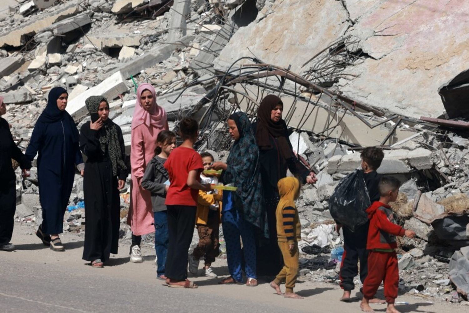 Donne e bambini palestinesi camminano vicino a un edificio distrutto da un bombardamento israeliano a Rafah, nel sud della Striscia di Gaza, il 31 marzo 2024