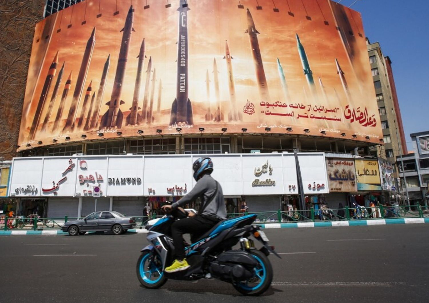 Un uomo passa in moto davanti a un cartellone pubblicitario che raffigura missili balistici iraniani in servizio a Teheran il 19 aprile 2024. I media statali iraniani hanno riferito di esplosioni nella provincia centrale di Isfahan
